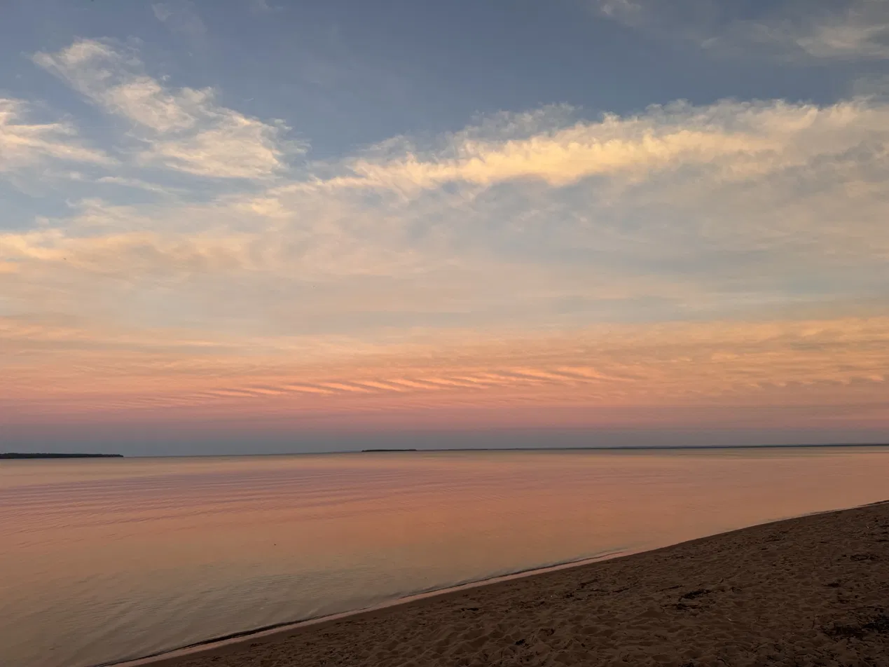 Sunset over Lake Superior from a sand beach on the Bayfield Peninsula, the sky striped pink and gold above still water.